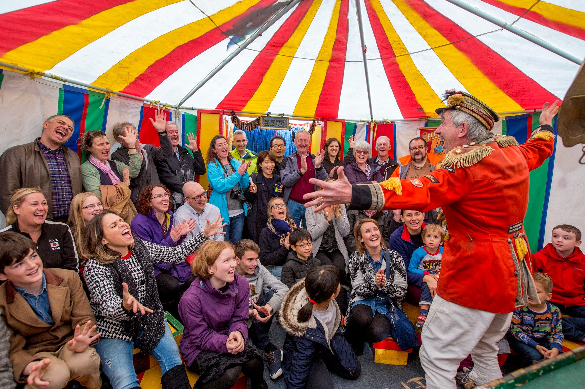 A man in circus costume performing to an audience in a colourful tent