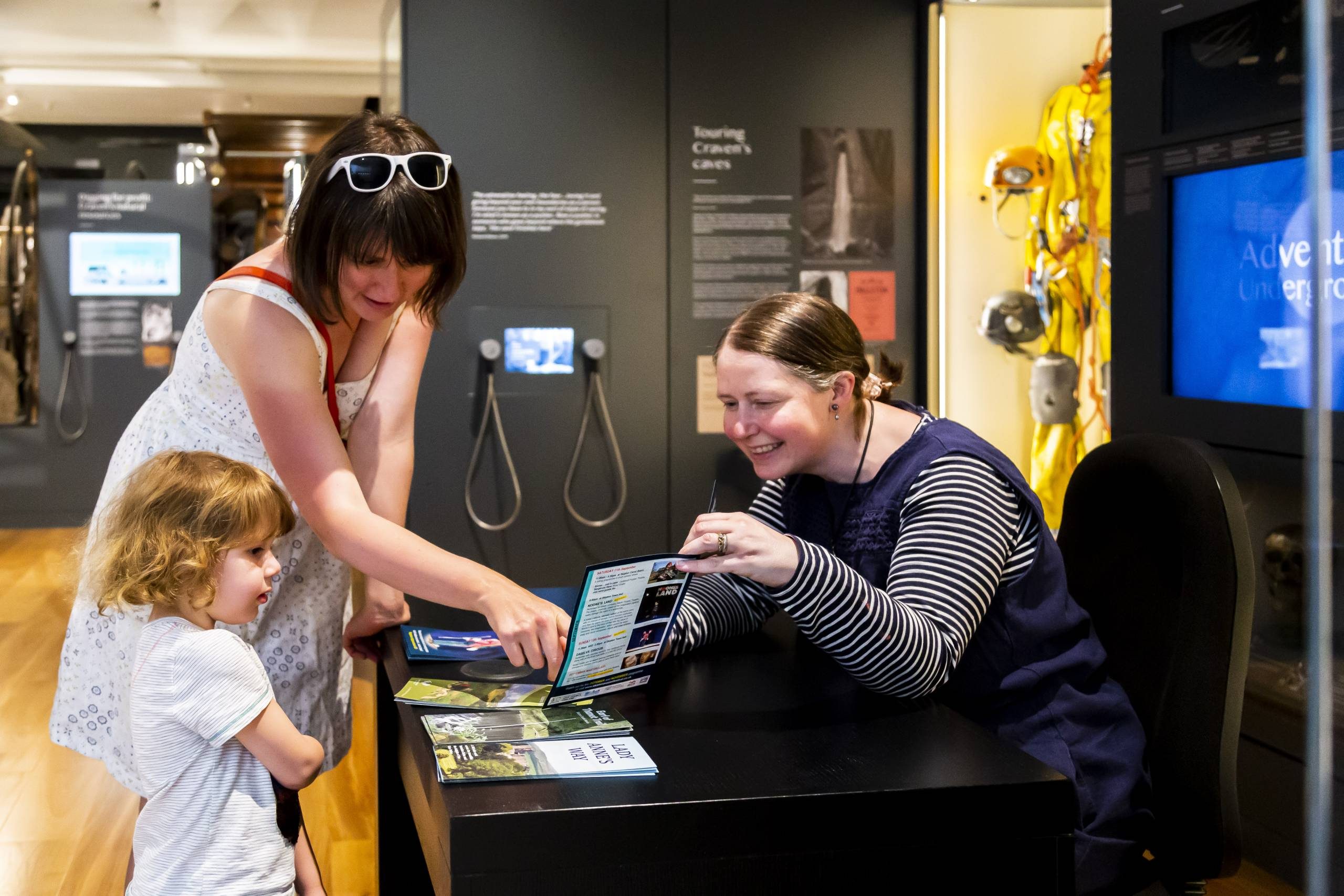 Museum staff talking to visitors and showing them a leaflet.