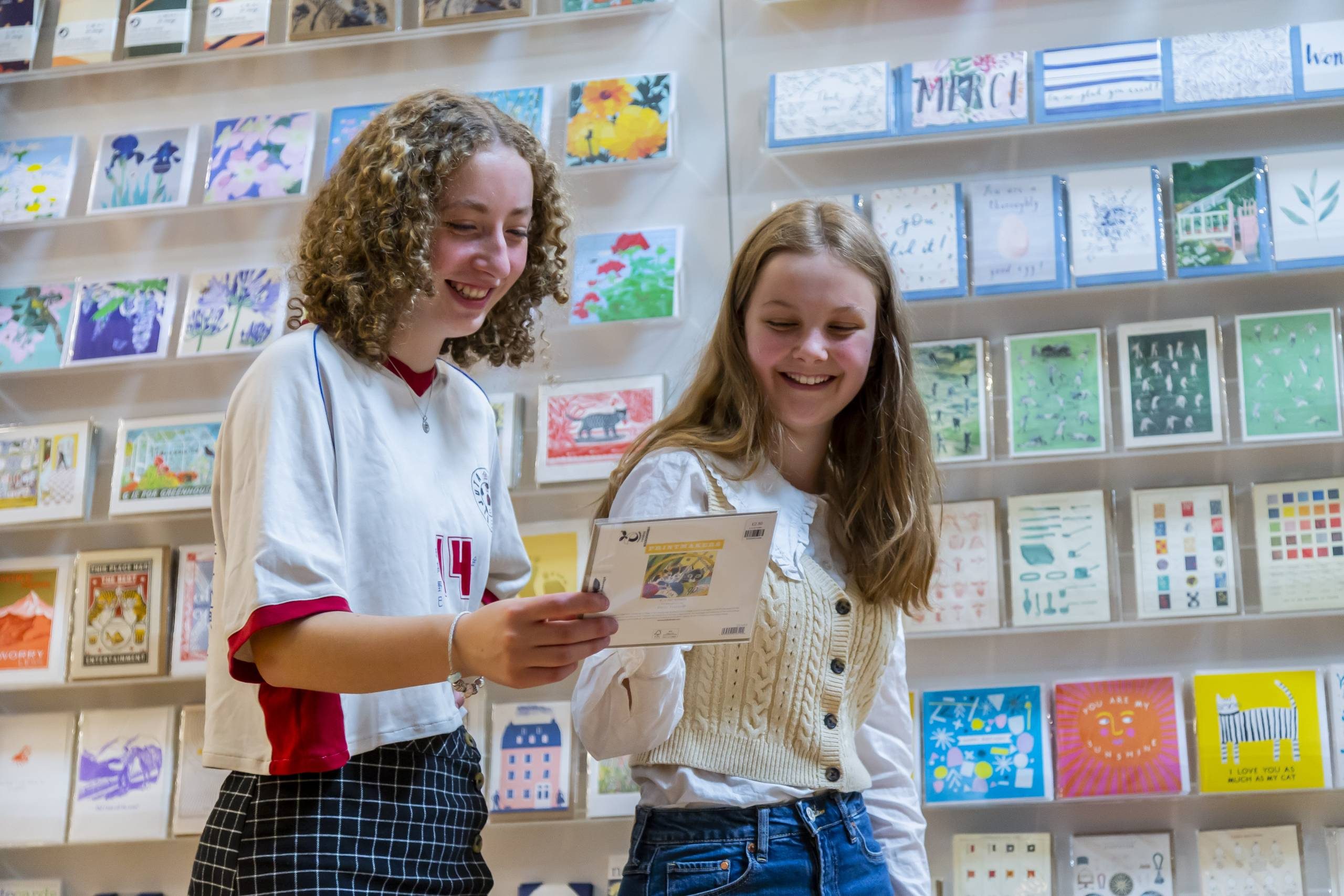 Two teenage girls looking at a greetings card and smiling.