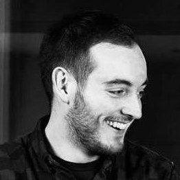 Man with short dark hair and a short beard. he is looking to the side and smiling.