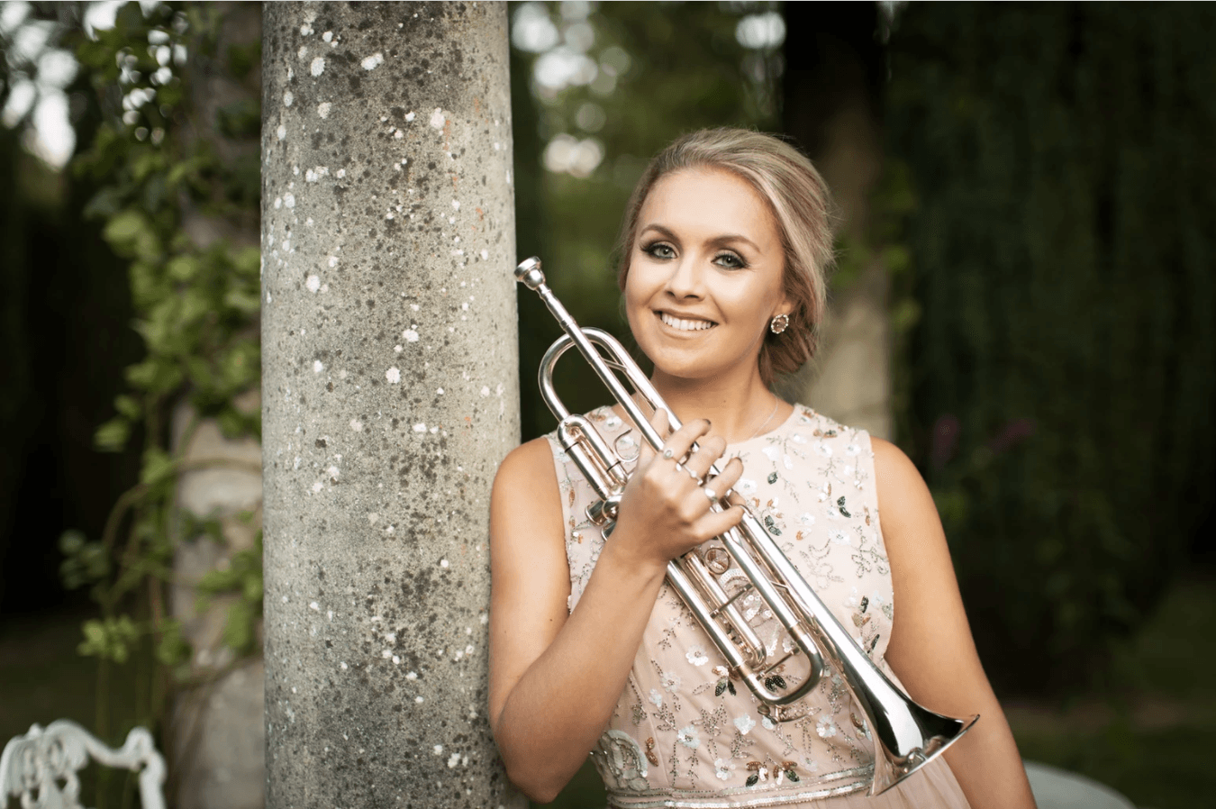 A woman leaning against a tree, holding a guitar.