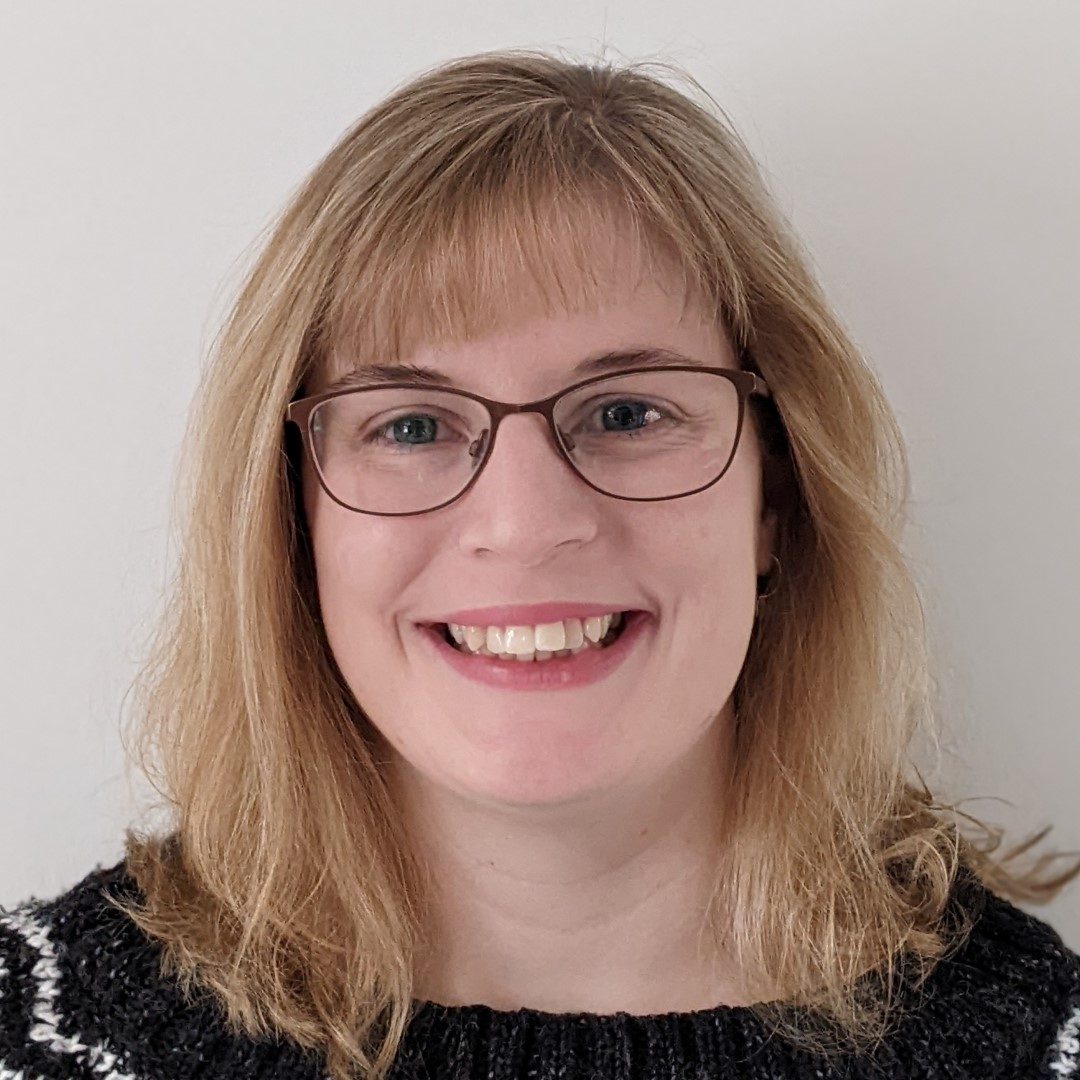 A woman with shoulder length blonde hair and glasses. She is smiling.